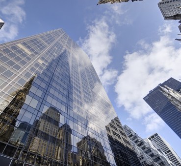 ofice buildings glass facade soaring towards the sky blue with patches of white clouds