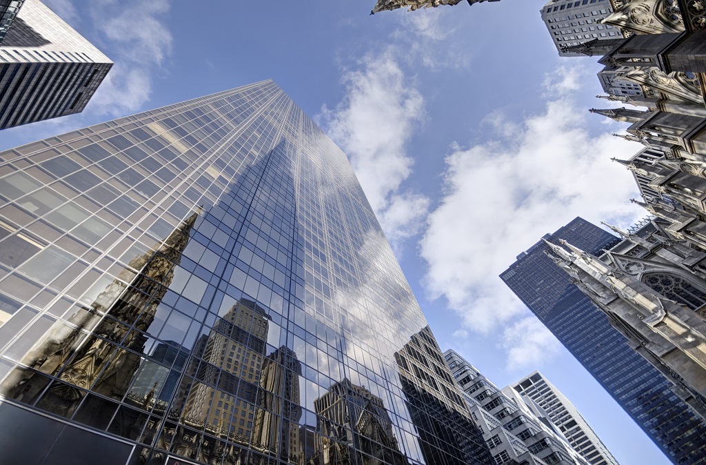 ofice buildings glass facade soaring towards the sky blue with patches of white clouds