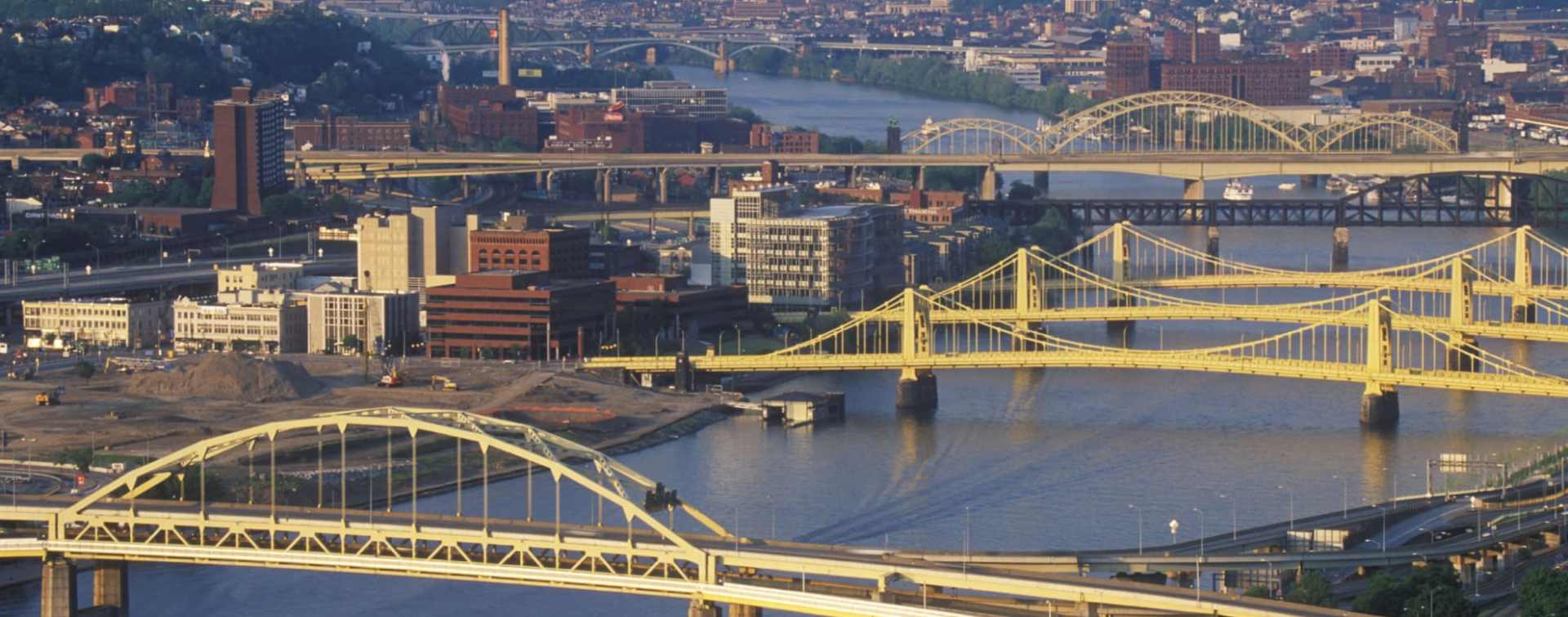 aerial view of Pittsburgh office buildings on the shore of the Allegheny river and of several of the city's bridges across the river.