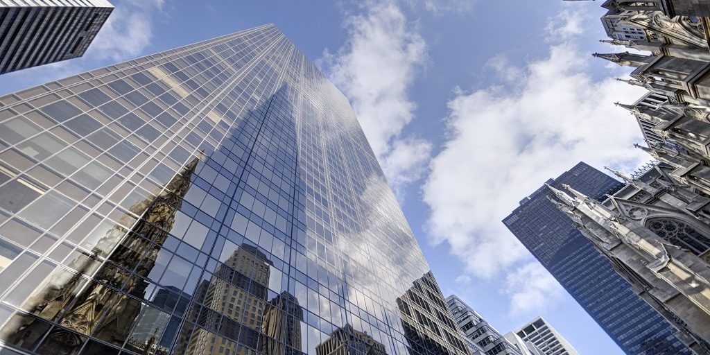 ofice buildings glass facade soaring towards the sky blue with patches of white clouds