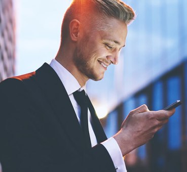 A businessman looking into his smartphone in front of an office building