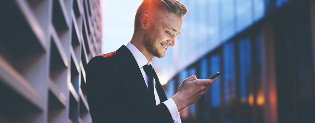A businessman looking into his smartphone in front of an office building